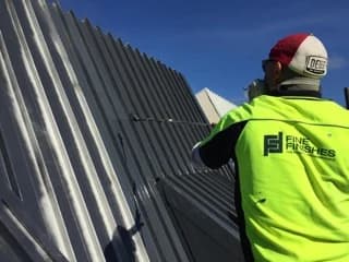Fine Finishes painter spray-coating a long-run metal roof