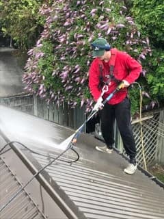 Painter pressure-washing a long-run metal roof before repainting